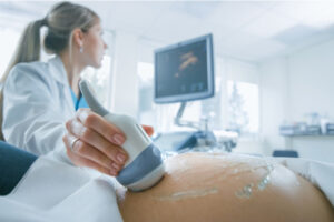 Nærbilde av lege som utfører ultralyd på gravid mage
