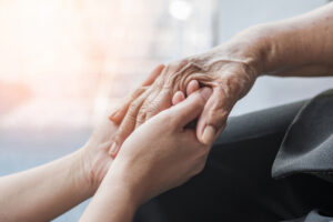 Nærbilde av en eldre persons hånd som blir holdt av et par yngre hender.