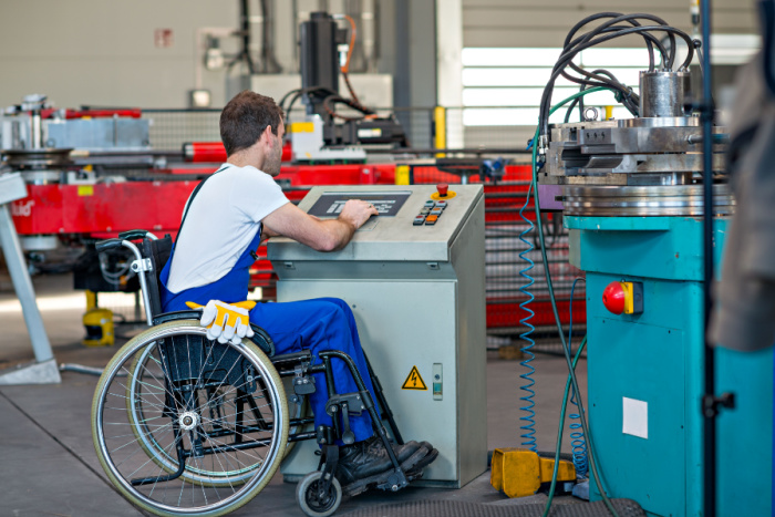 Funksjonshemmet arbeider i rullestol som betjener en maskin i sitt arbeide