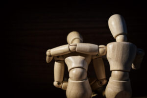 Bilde viser to tre-figurer som sitter ved siden av hverandre som illustrerer en person som lener seg framover, hvor den andre holder armen rundt rundt skuldrene til den andre.