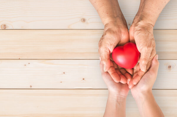 Fotografi ovenfra av to hender som sammen holder ett rødt hjerte.
