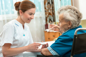 Bilde av kvinneig pleier som gir medikamenter til eldre dame i rullestol