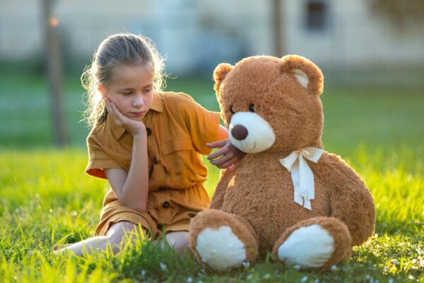 Fotografi av barn med teddybjørn, sittende på gresset om sommeren.