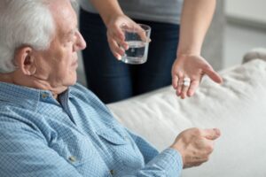 En hjelper deler ut medisiner til en eldre mann