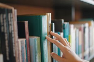 Bilde av hånd som blar gjennom bøker i bokhyller Foto: Shutterstock