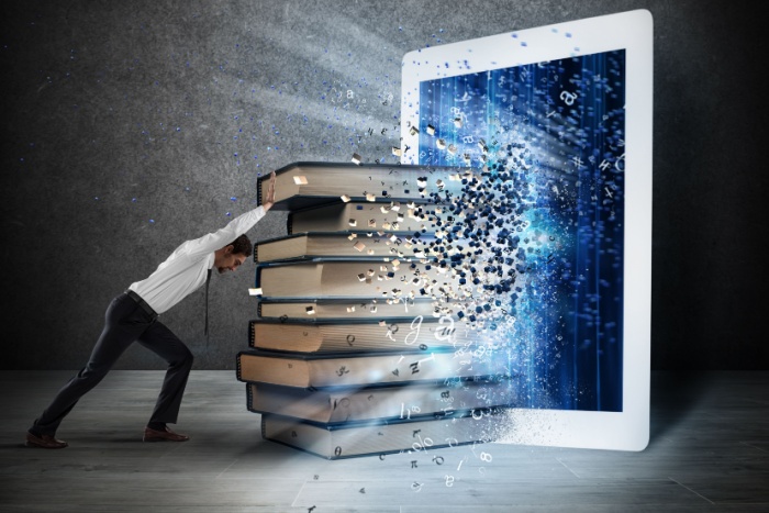 Shutterstock_611253707 Mann som dytter en stabel med bøker mot en nettbrett