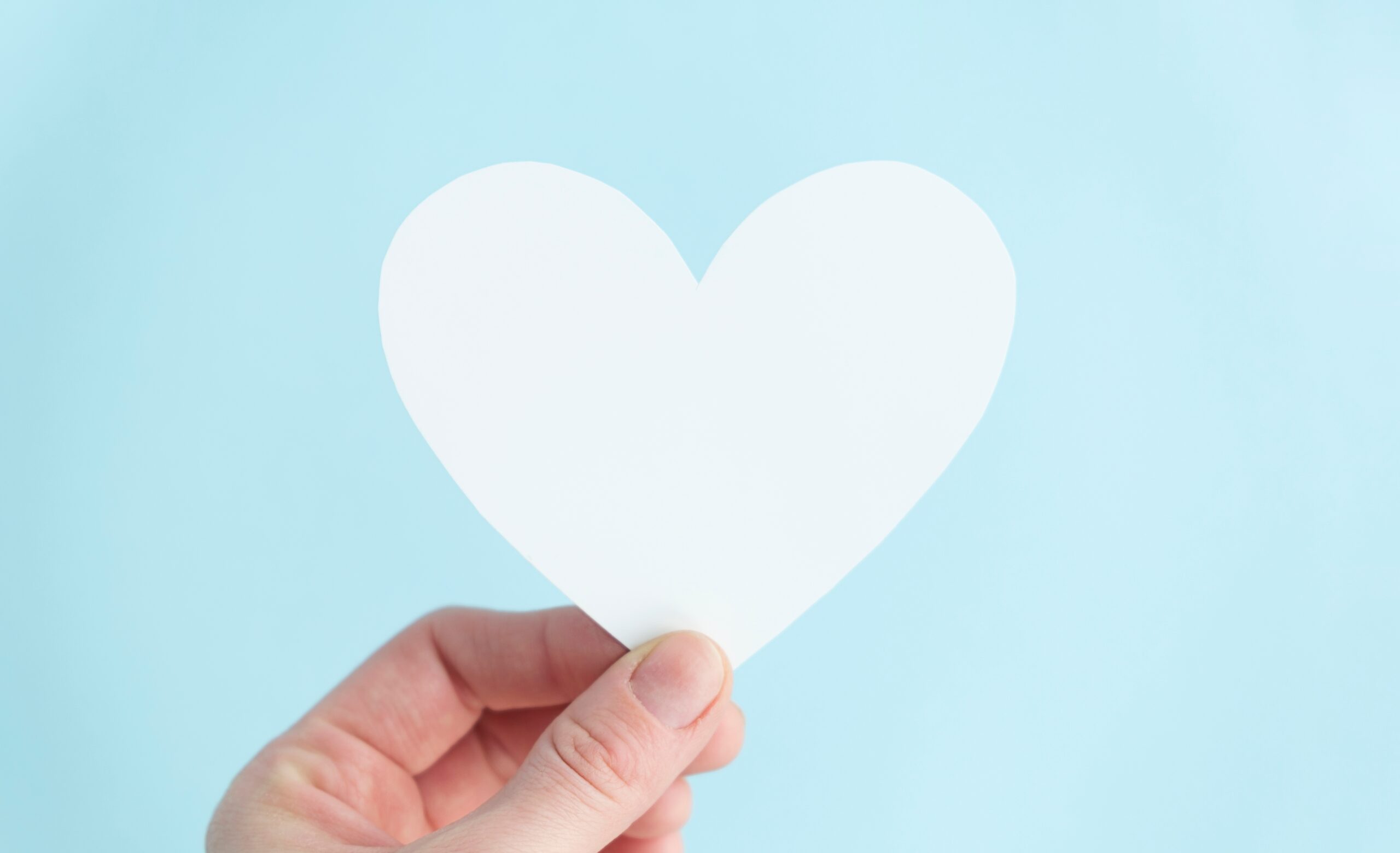 Hand,Holding,A,White,Heart,In,Blue,Background.,Charity,,Pure Fotografi av person som holder oppe hjerteformet papir, blå bakgrunn