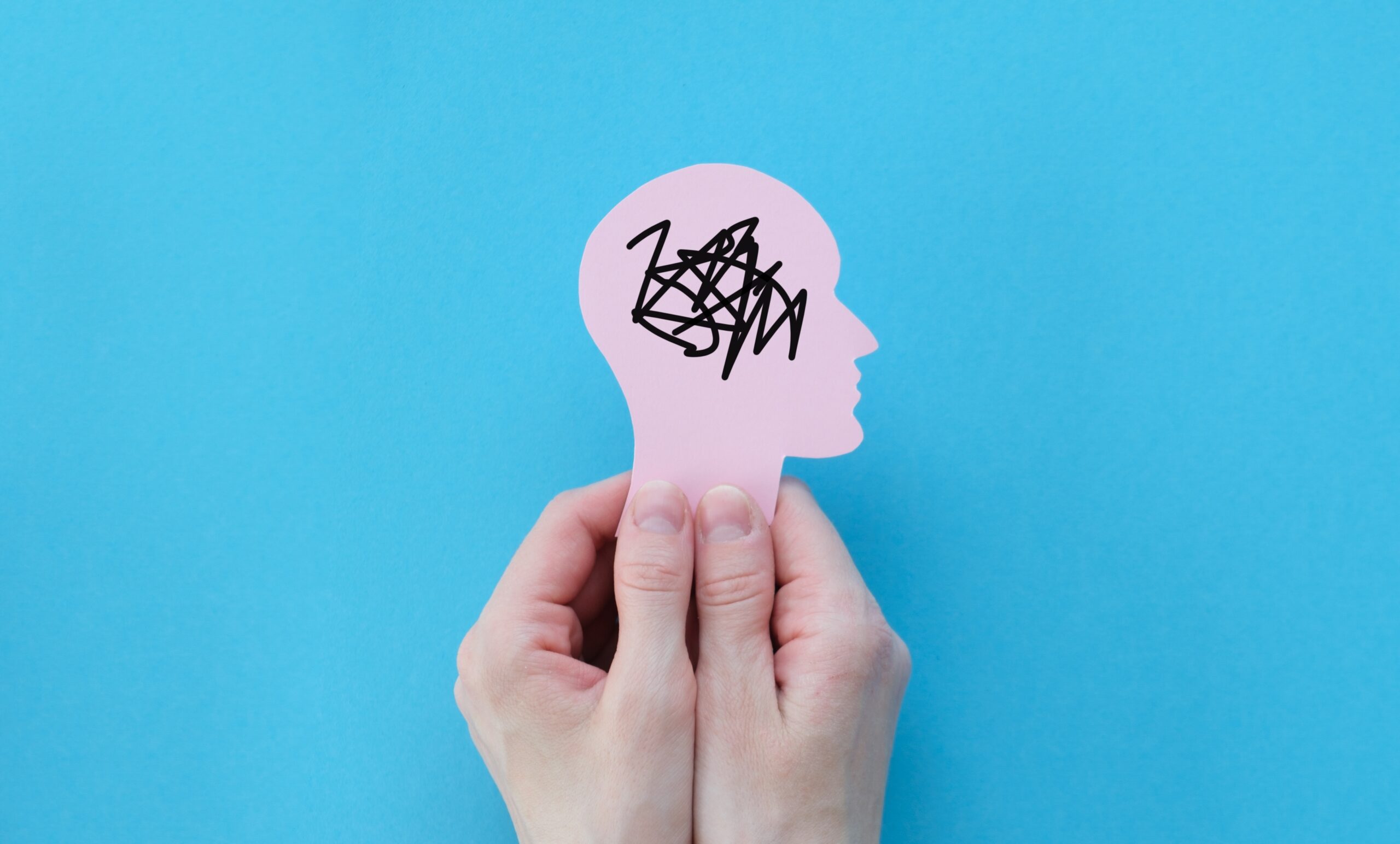Hands,Holding,Human,Head,,Attention,Deficit,Hyperactivity,Disorder,,Adhd,Symptom, Hender som holder en figur av et hode i profil, med krusseduller i hodet, blå bakgrunn