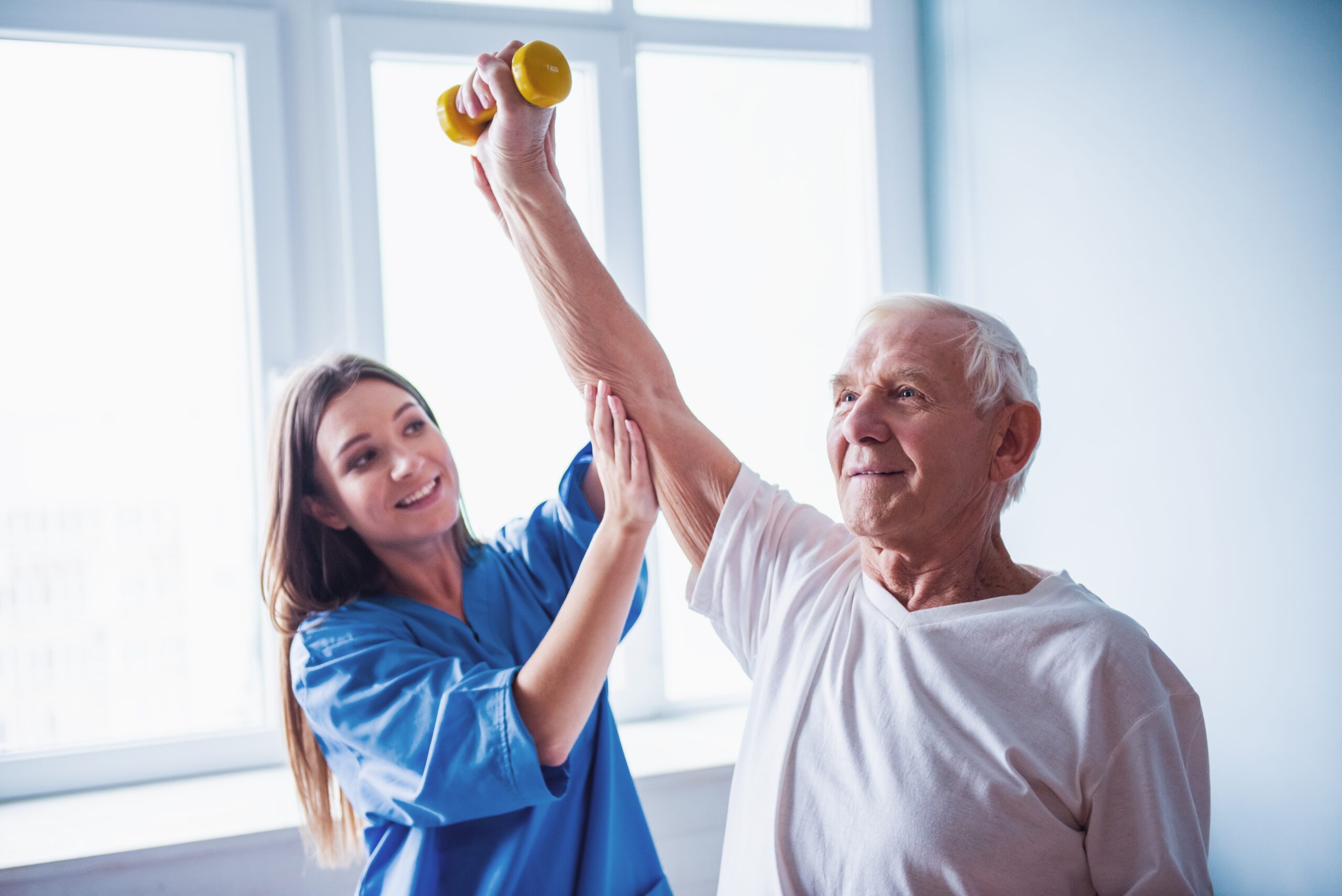 Handsome,Old,Man,Is,Doing,Exercises,With,Dumbbells,And,Smiling, Fotografi av helsepersonell og eldre mann. Rehabilitering i fokus