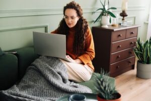 Bilde av kvinne sittende i sofa med laptop på fanget.