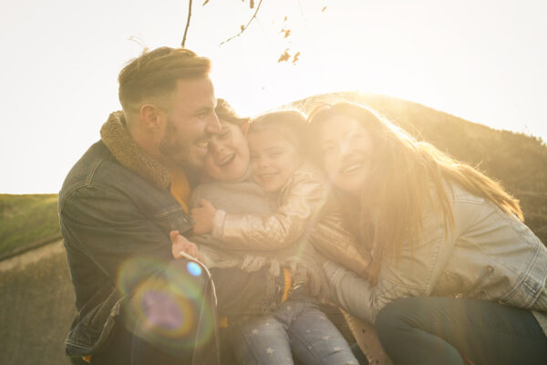Fotografi av familie, sittende sammen, klemmer hverandre utendørs i sola