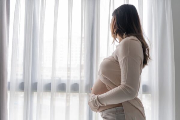 Gravid kvinne som holder seg på magen og ser ut av et vindu