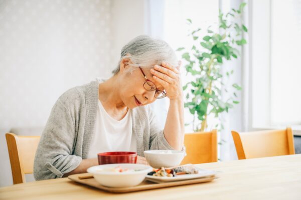 Fotografi av eldre dame, sittende ved middagsbordet som tar seg til hodet