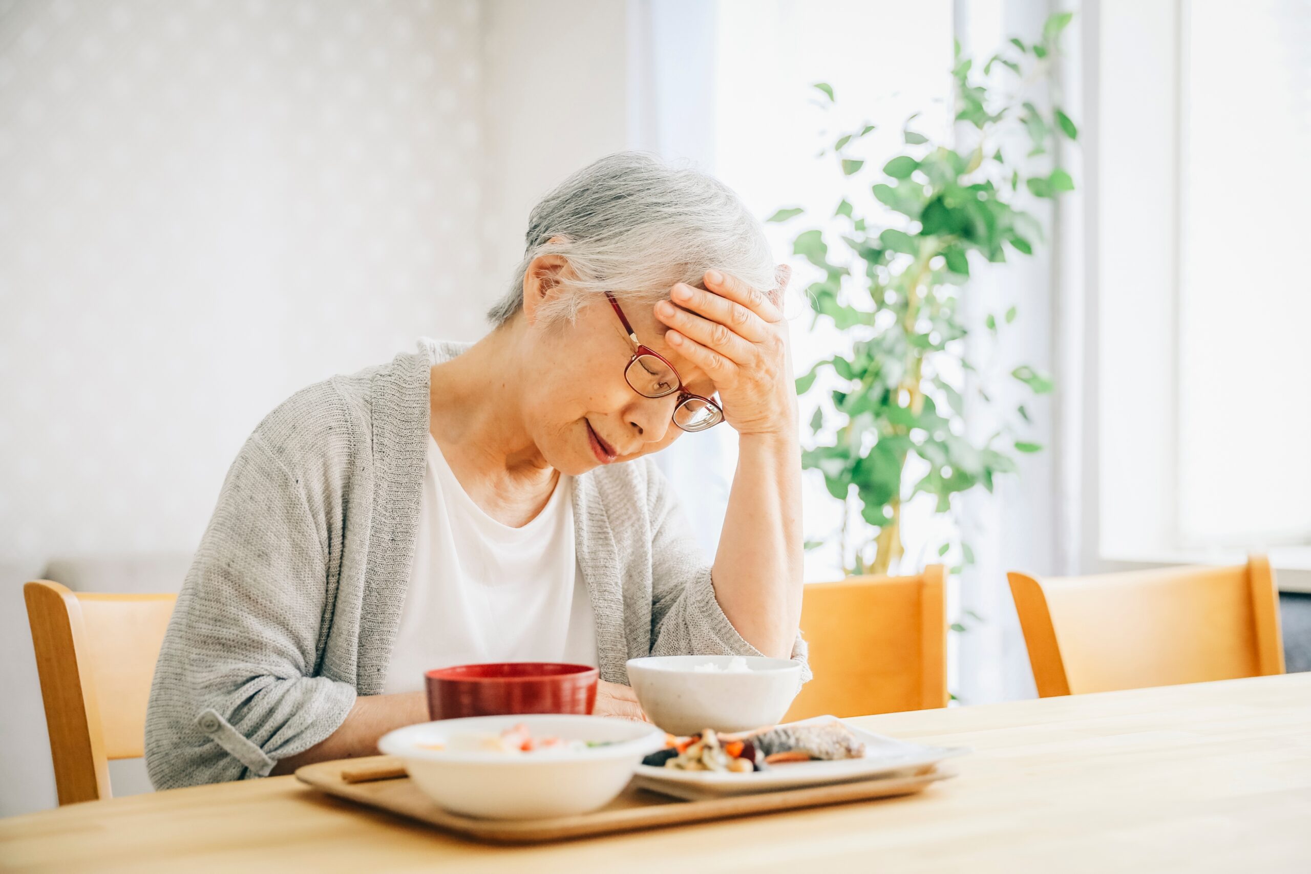 Elderly,Woman,Eating,A,Meal,Without,Energy Fotografi av eldre dame, sittende ved middagsbordet som tar seg til hodet
