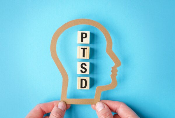 Bildeillustrasjon som beskriver PTSD. Fingre holder en figur formet som et hode i profil over terninger som staver PTSD