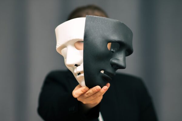 Person som holder to masker foran ansiktet. En hvit og en svart maske.