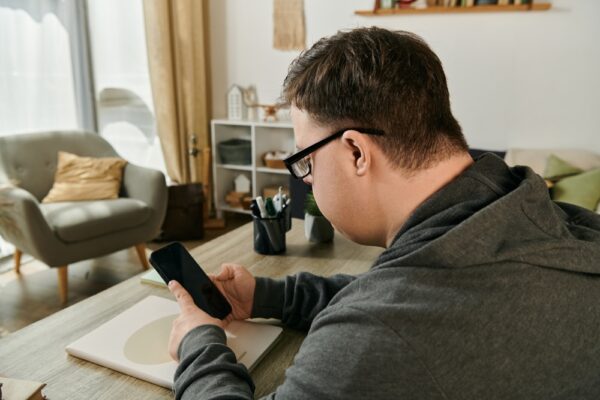 Fotografi av voksen person med down syndrom, sittende ved et bord på mobilen sin