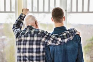 Fotografi av eldre mann som holder armen over skulderen til en yngre mann. Bilde bakfra