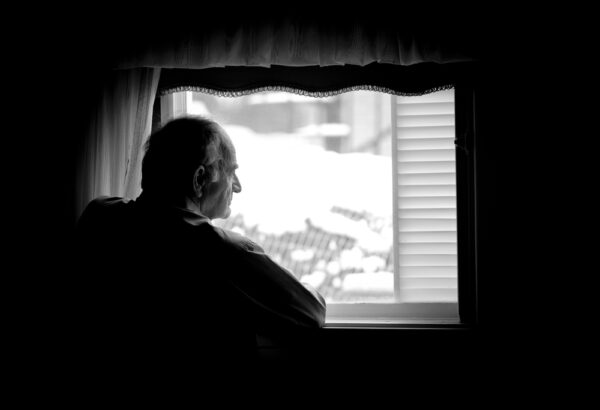 Fotografi av eldre man som ser ut av vinduet. Fotografiet er svart hvitt