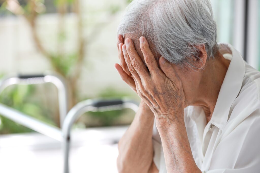 Eldre dame som er trist, sitter framoverlent og holder hendene foran ansiktet sitt.