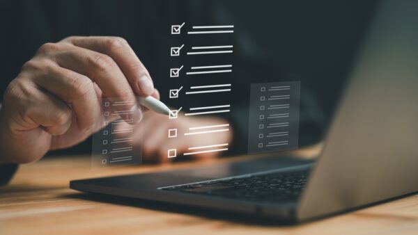 Bildeillustrasjon av en hånd som holder digital penn opp foran laptop, og huker av en liste bokser