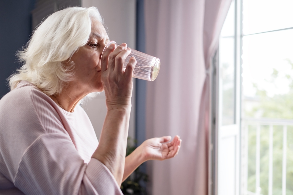 Senior,Woman,Takes,Pill,With,Glass,Of,Water,In,Hand. Fotografi av eldre dame som tar medisiner, og drikker vann