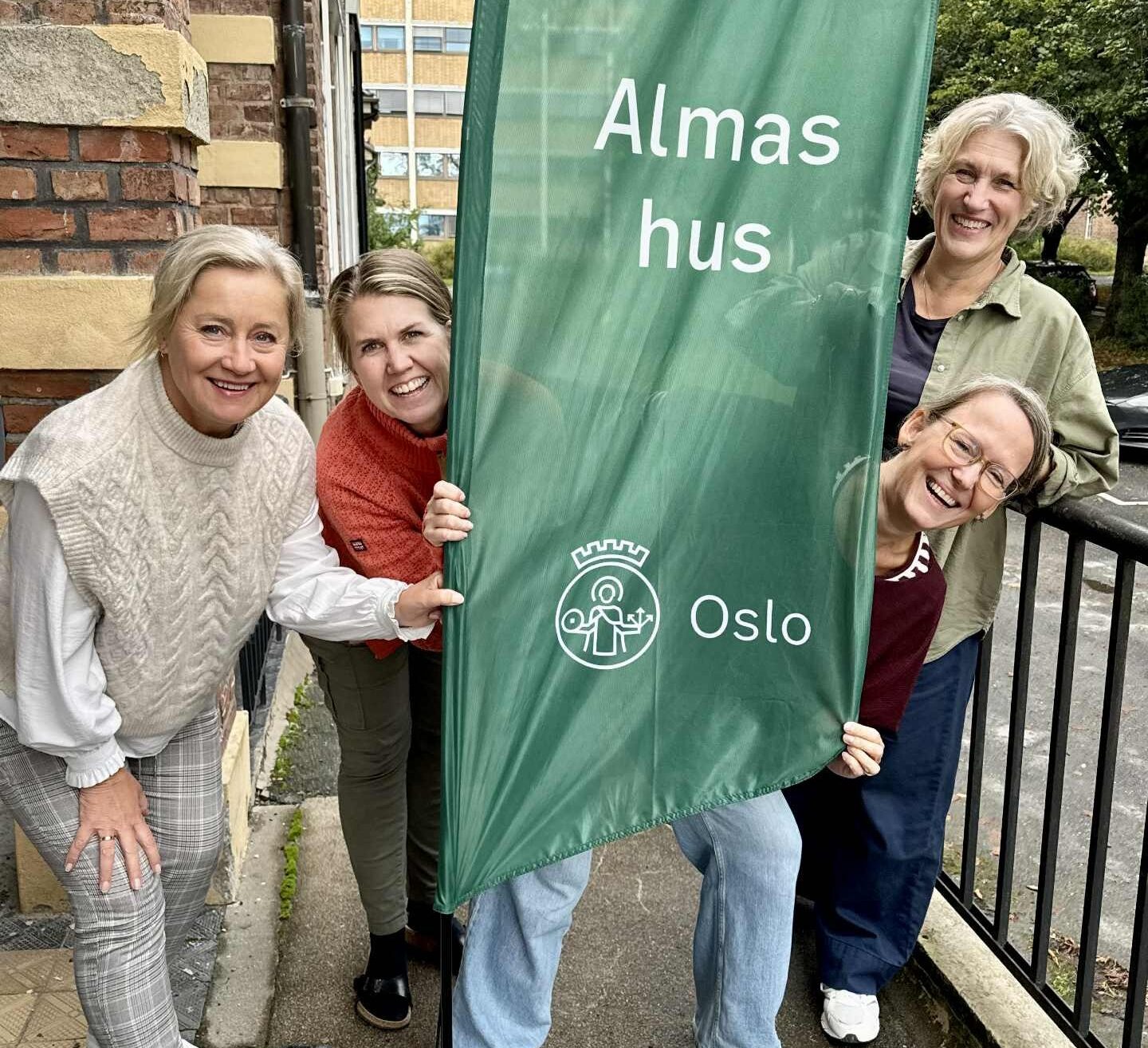 Bilde-Almateamet fotografi av fire damer utenfor almas hus, stående bak en vimpel