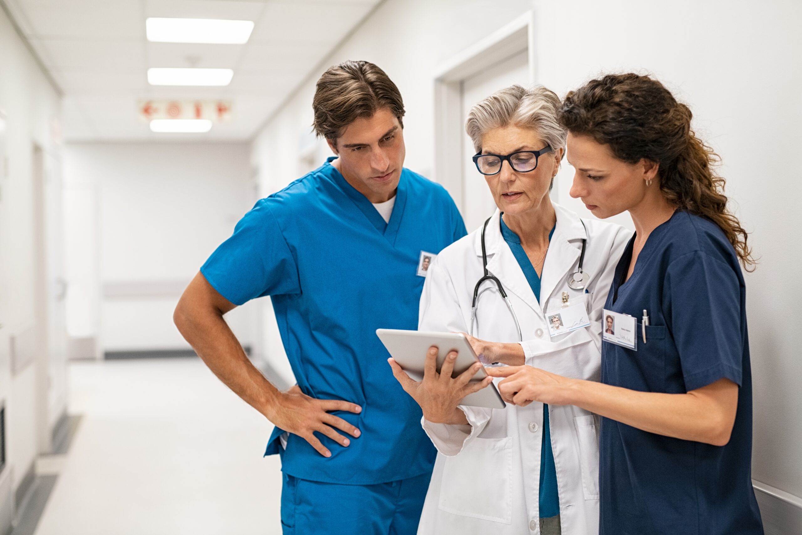 Mature,Female,Doctor,Discussing,Medical,Report,With,Nurses,In,Hospital fotografi av helsepersonell som konfererer, i en sykehus gang