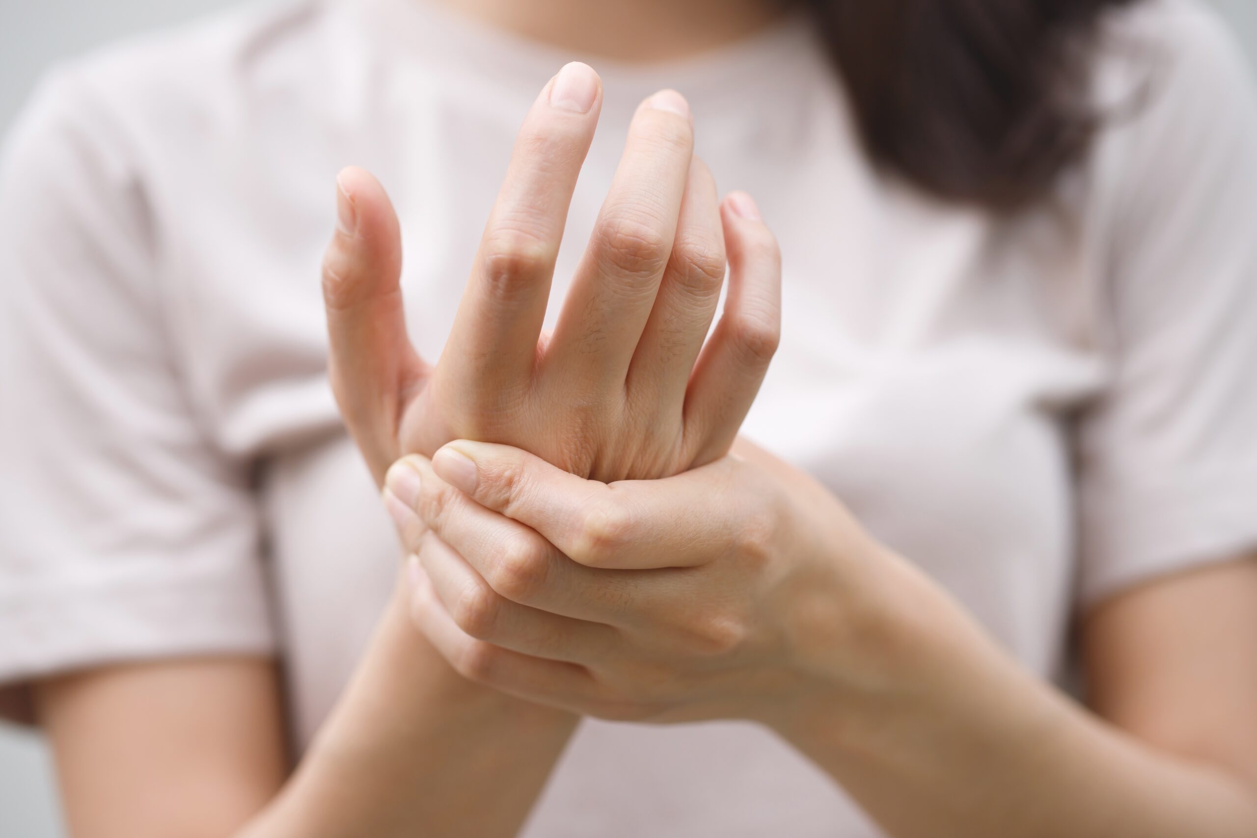 Osteoarthritis,Is,A,Common,Cause,Of,Hand,Joint,Pain,In fotografi av kvinne som tar seg til hånden i betydelig smerte. Hvit t skjorte, brunt hår, griper høyre hånd hardt med venstre.