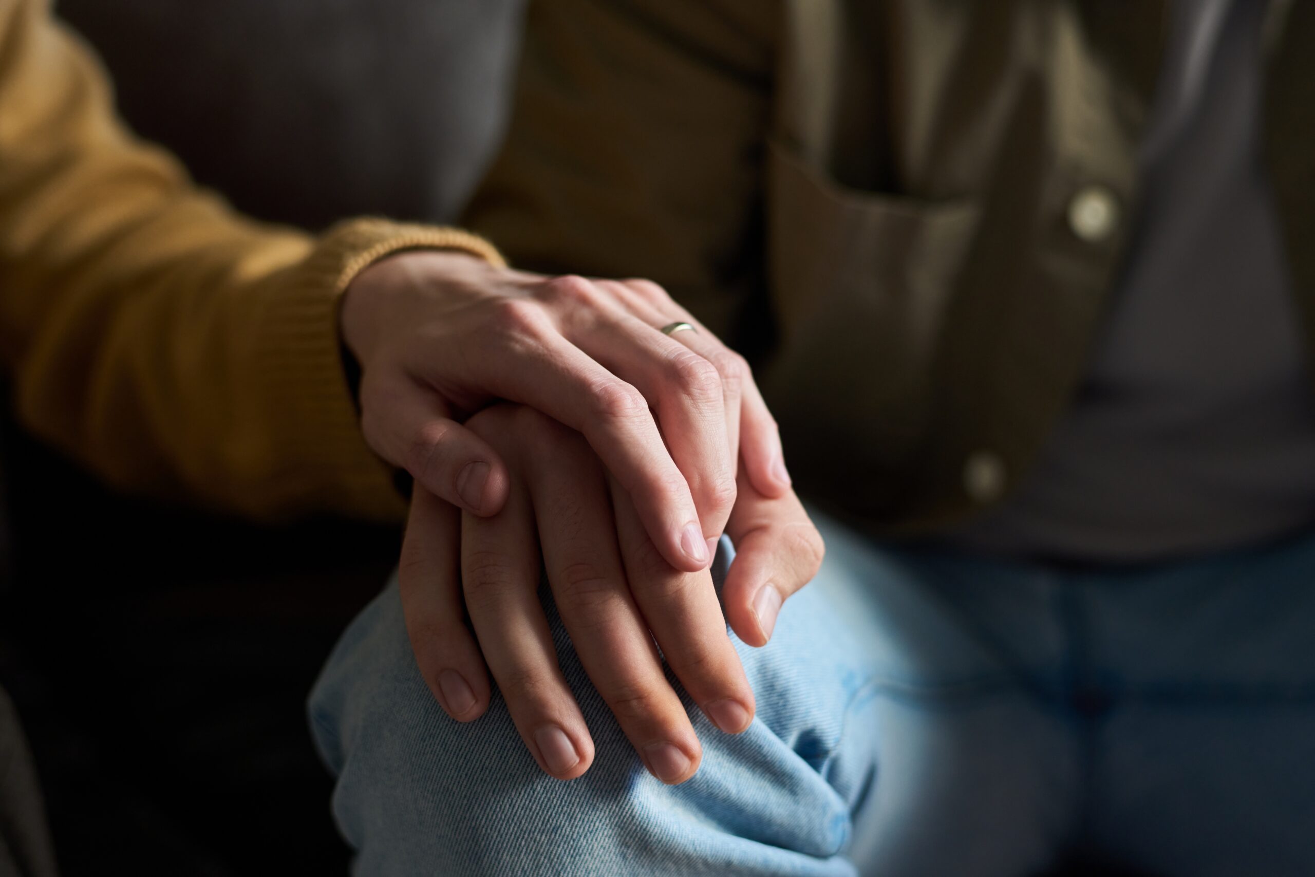Caucasian,Young,Adult,Woman,Gently,Placing,Hand,On,Knee,Of Fotografi av et par som holder hender, mørke skygger, litt lys på kneet hvor kvinnen holder hånden sin over mannen, på hans kne