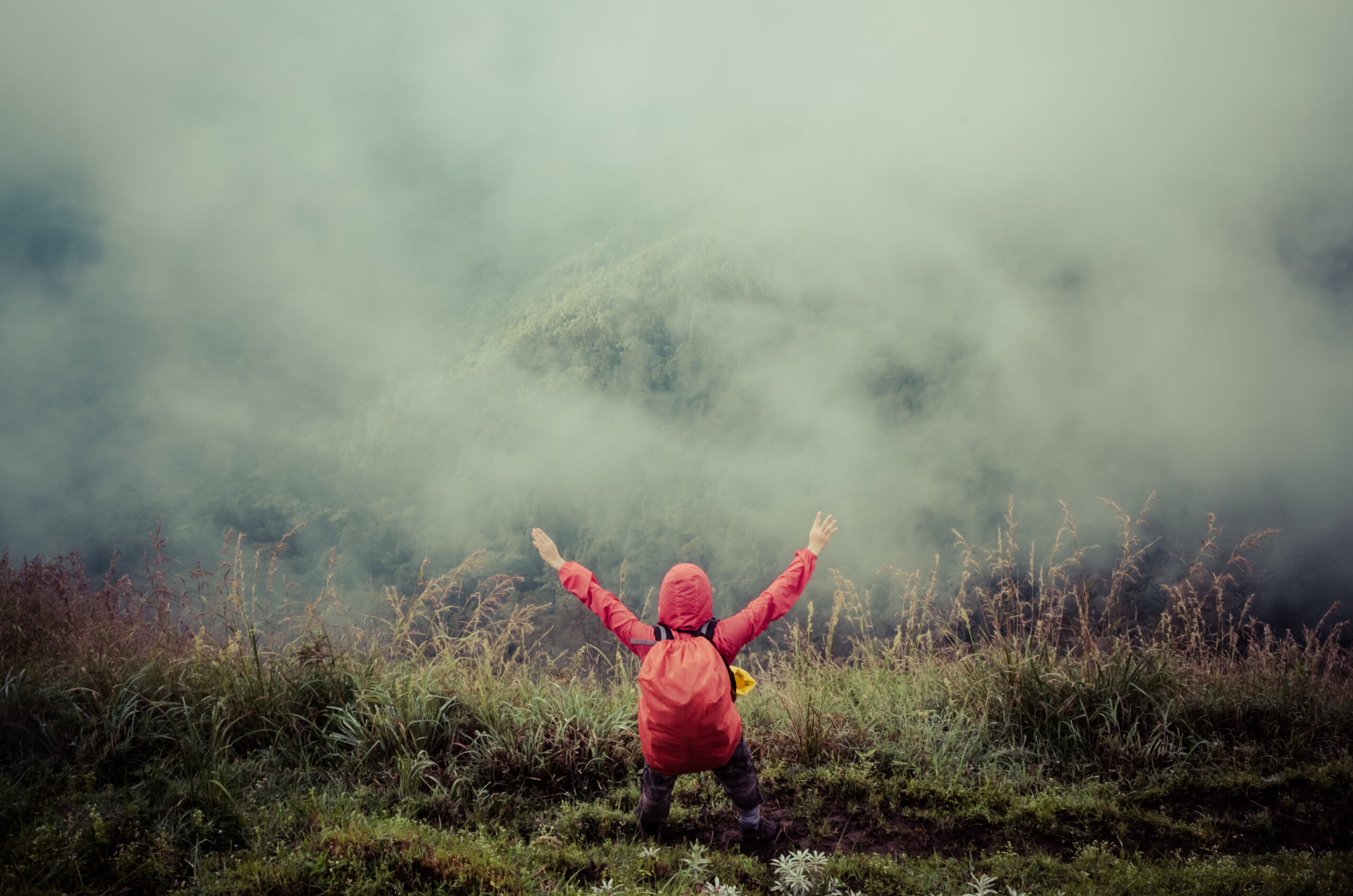Man,With,Backpack,Standing,On,A,Hill,In,Foggy,Weather Fotografi av person på et fjell som strekker armene ut i været, tåkete, rød jakke