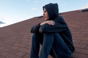 Illustrasjonsbilde av tenåringsgutt som sitter på hustak og ser ut over. I bakgrunnen er det blå himmel.