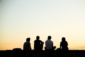 Illustrasjonsbilde av fire tenåringer sittende på bakken med ryggen til omslynget av en lys himmel.