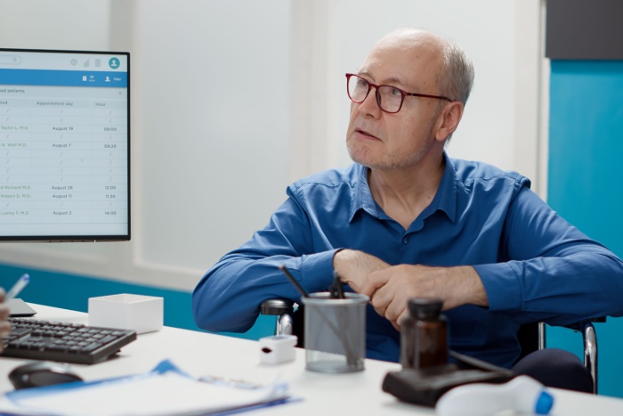 Mann i rullestol snakker med lege på kontor