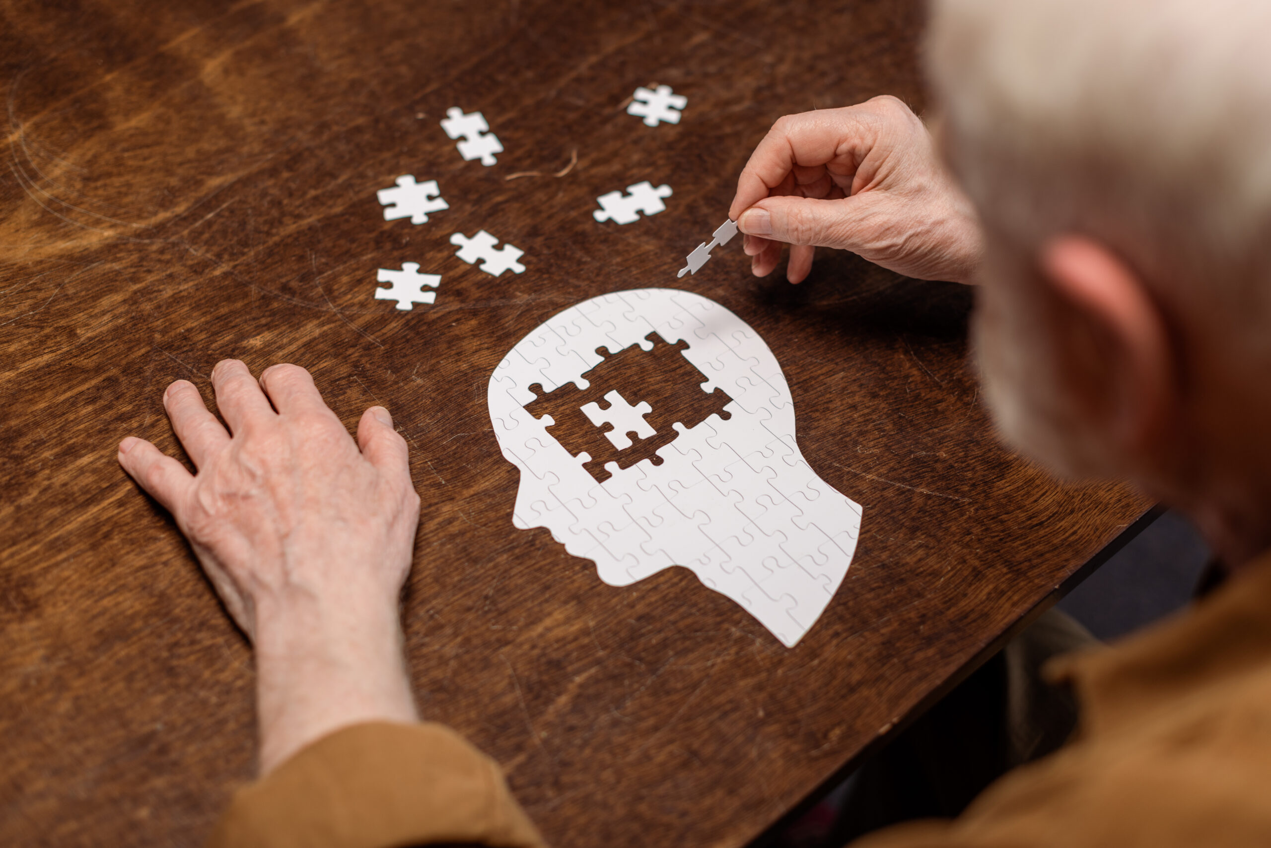 High,Angle,View,Of,Senior,Man,Collecting,Jigsaw,Puzzle,As Fotografi av eldre mann som pusler puslespill. Puslespillet er et menneskehode i profil