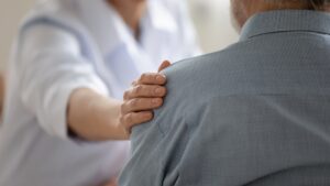 Helsearbeiders støttende hånd på skulderen til en mann