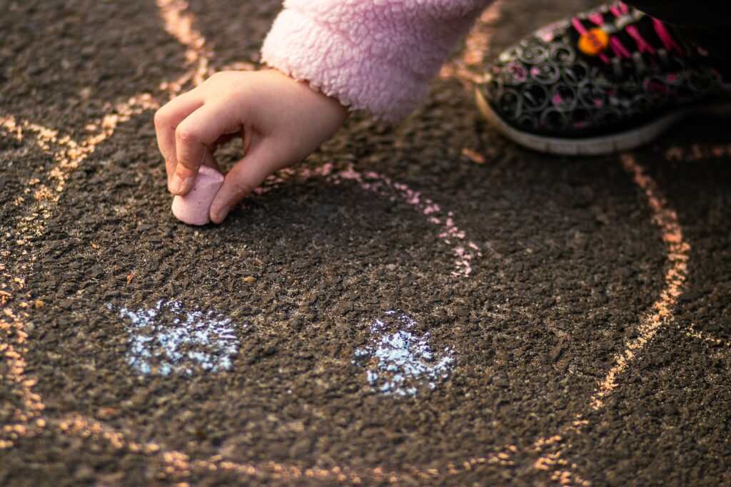 Barnehånd som tegner et smilende fjes med kritt på asfalten.