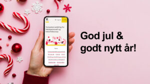 Hånd som holder en mobil. Julepynt i bakgrunn. Tekst som sier god jul og godt nytt år.
