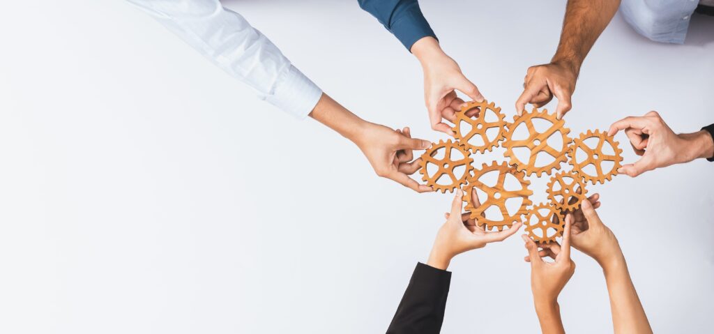Flere hender holder et tannhjul. Visualiserer å holde tannhjulene i gang. Teamwork.
