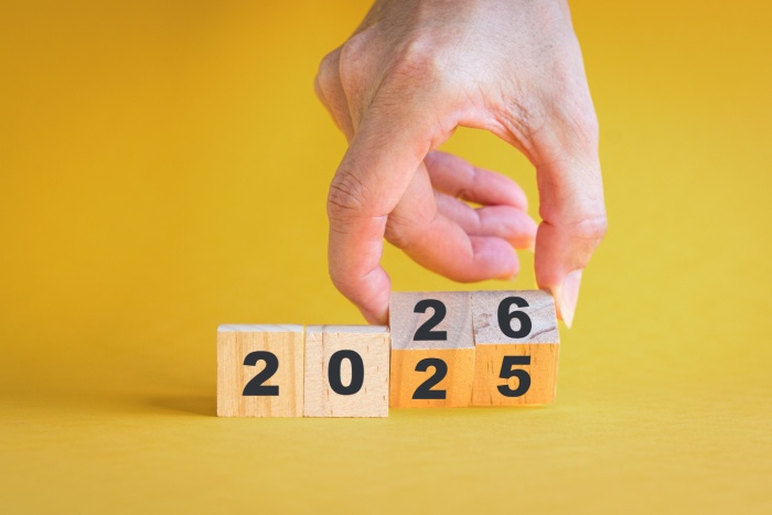 En hånd som vender tallet 25 til 26 på gul bakgrunn