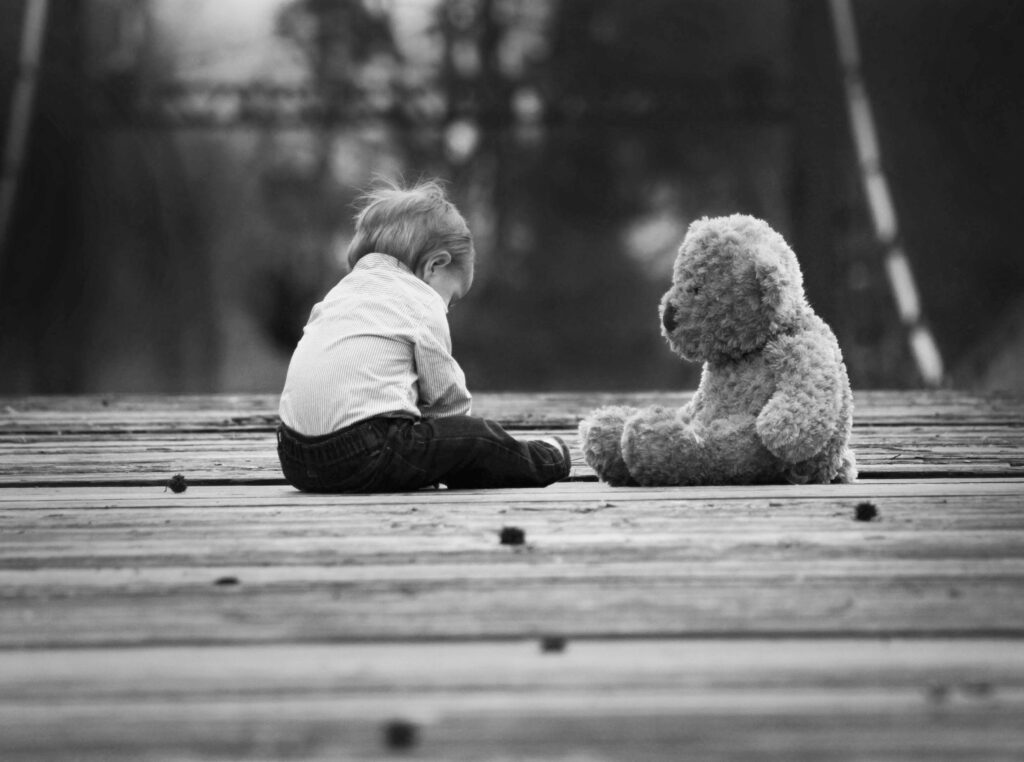 Lite barn som sitter ovenfor en bamse