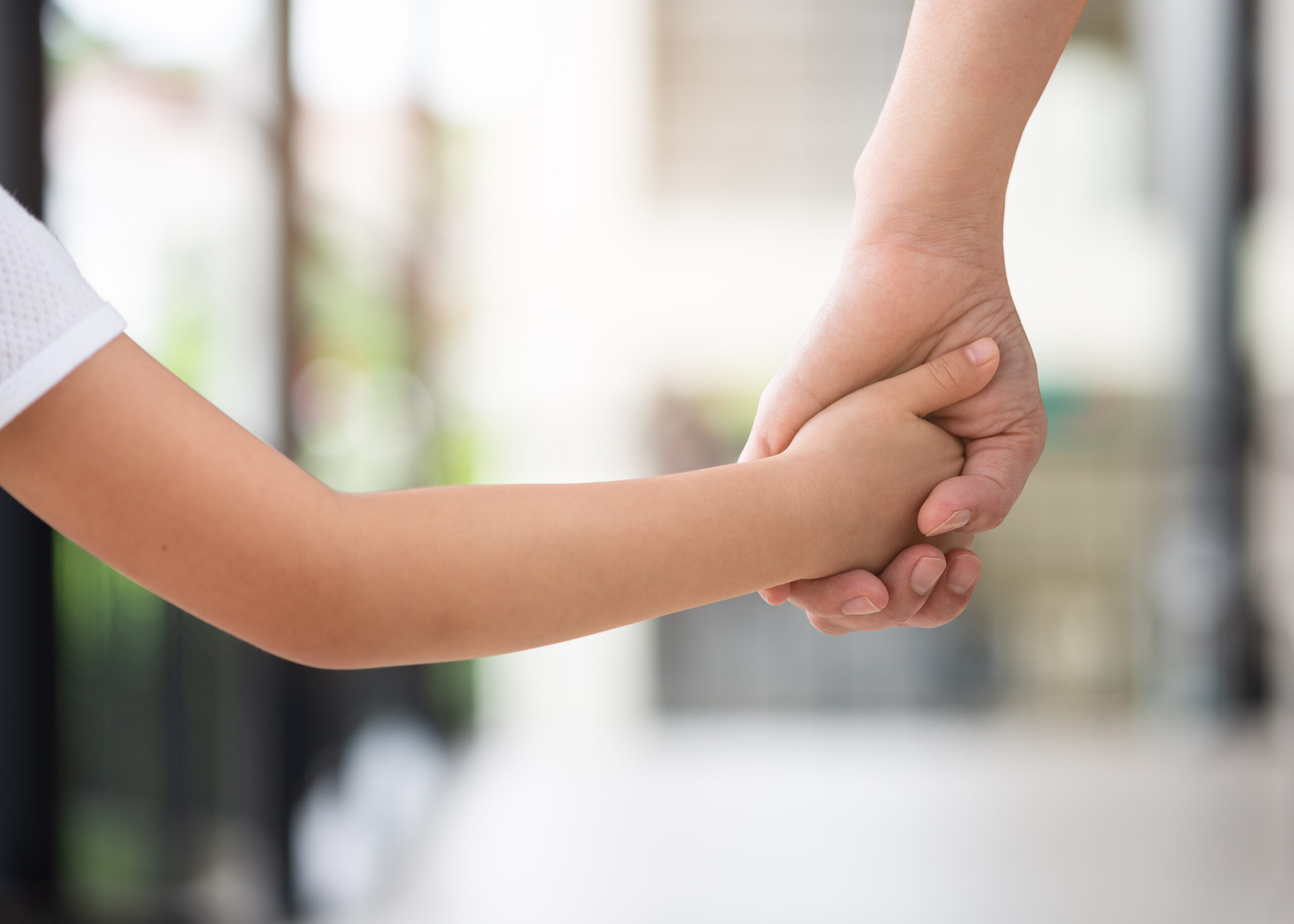 Nærbilde av barn som holder voksen i hånda, lyst og sommerlig