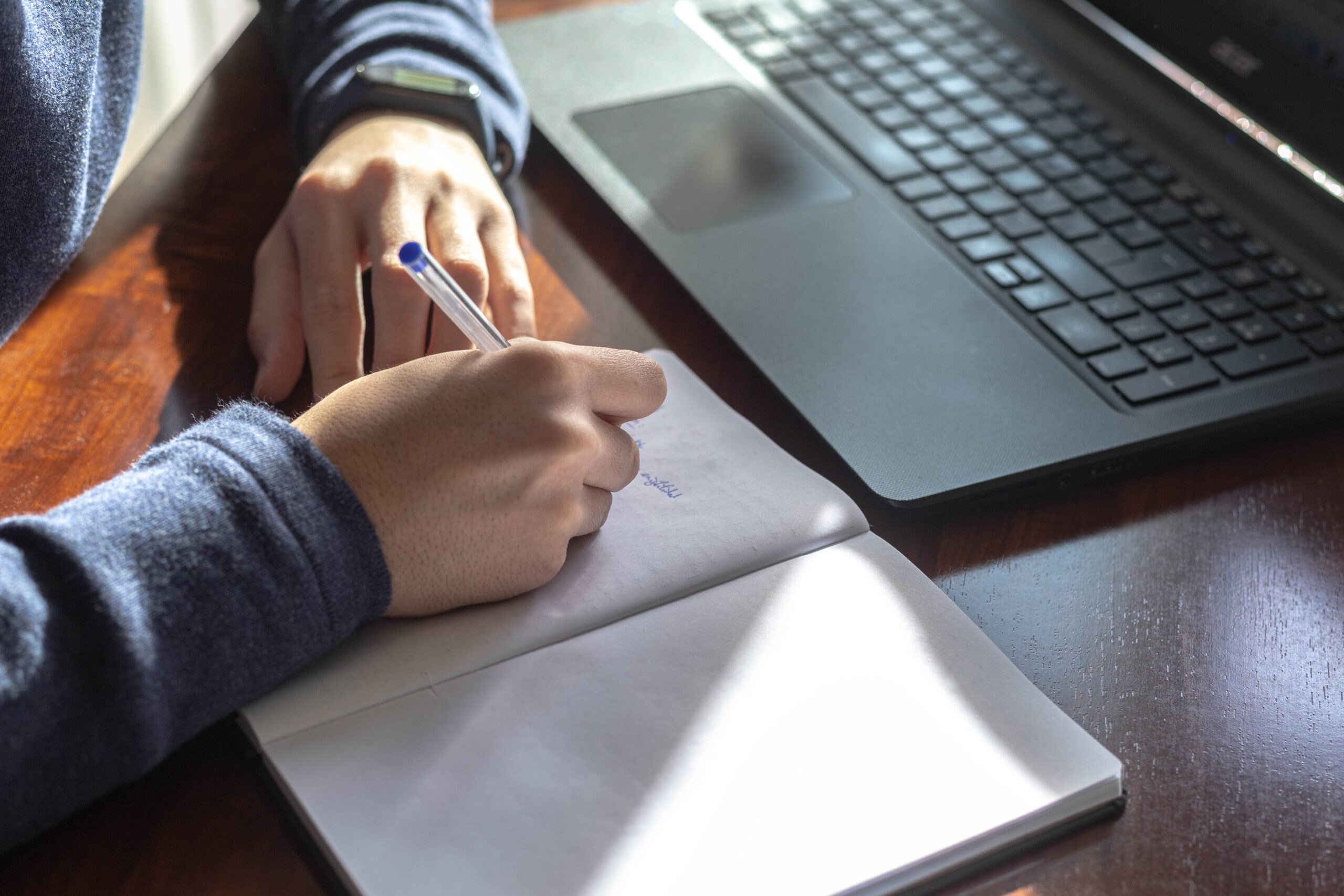 fotografi av person sittende med notatblokk og penn, foran en pc