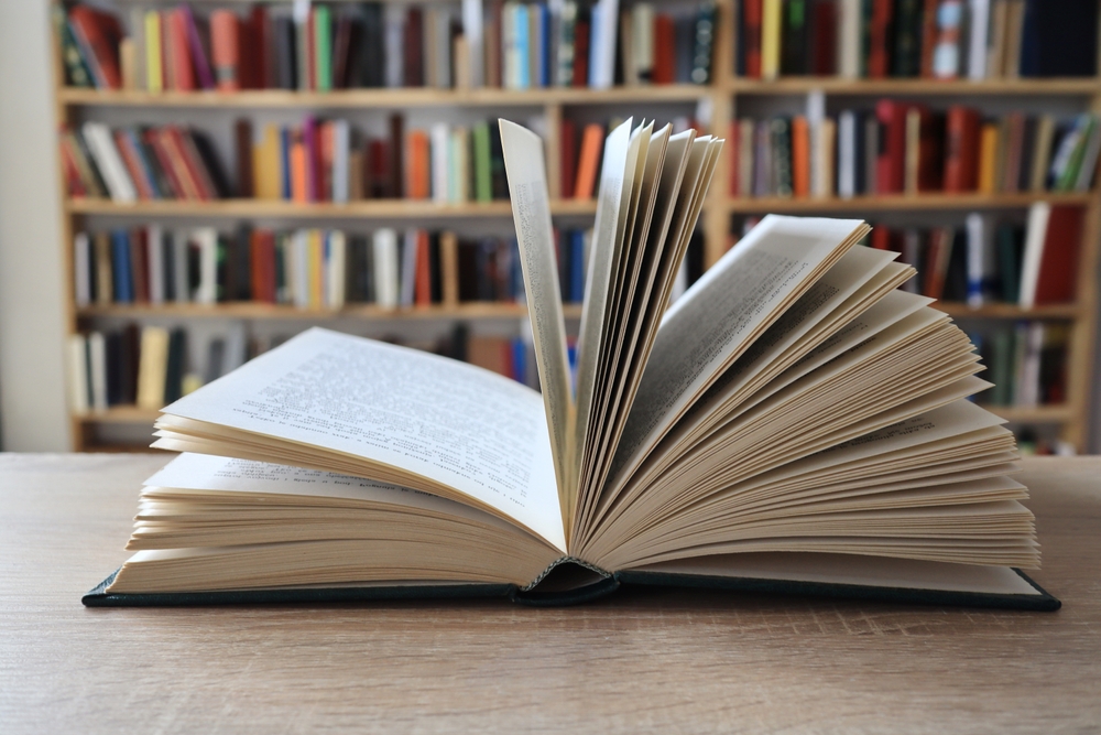 Fotografi av åpen bok, liggende på et bord i et bibliotek