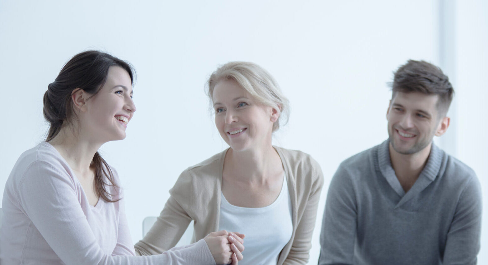 Fotografi av tre mennesker i dialog-møte, smilende, blide, hvi bakgrunn, to kvinner og en mann