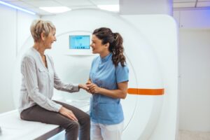 En sykepleier holder en dame i hånden. damen sitter på en benk og skal ta røntgen.