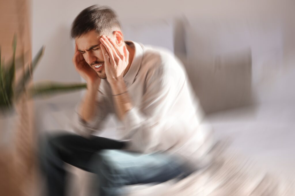 Ung mann i mental ubalanse som sitter på en seng og tar seg til hodet.