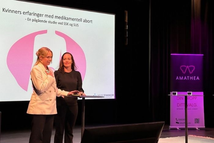 Fotografi tatt på tidligere Amathea fagdag, konferanse-setting ned to fordragsholdere på en scene