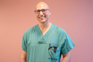 fotografi av podkast-gjest Faraz Afzal, stående i lege-antrekk foran en beige vegg