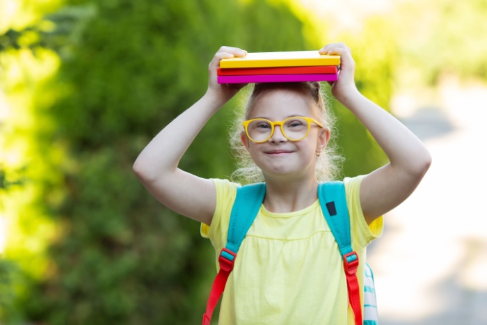 Jente med Downs syndrom bærer bøker på hodet